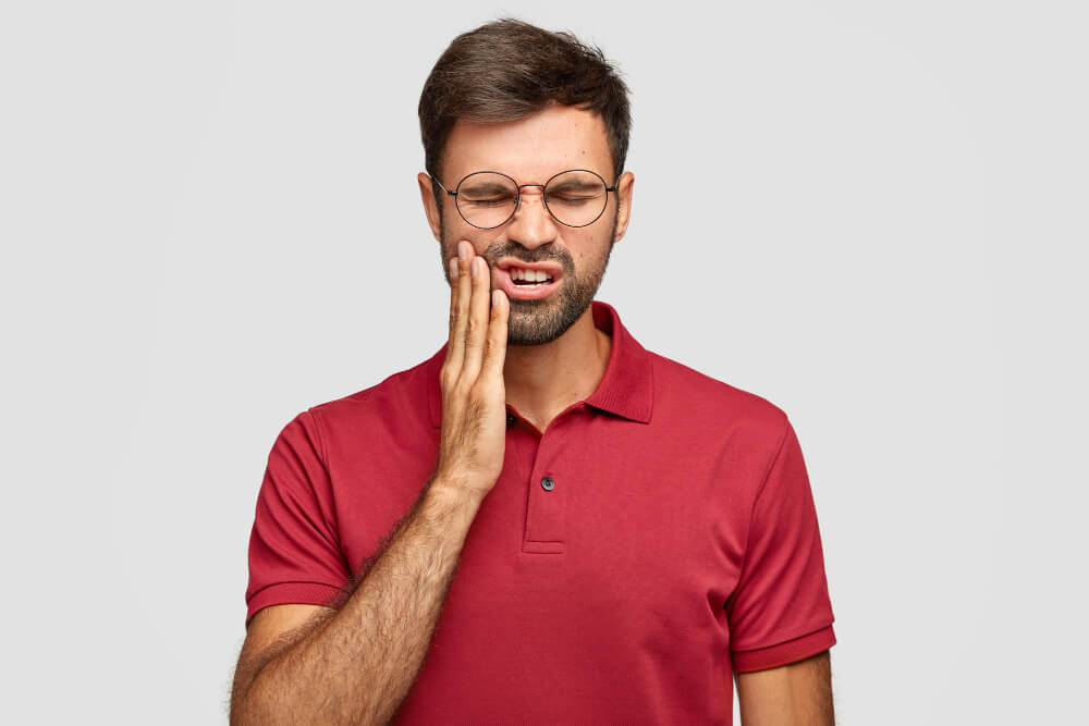 Man experiencing wisdom tooth pain holding jaw in discomfort and swelling