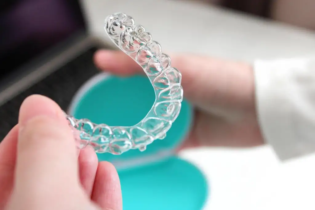A patient holding a transparent invisible braces dental aligner next to a laptop and protective case